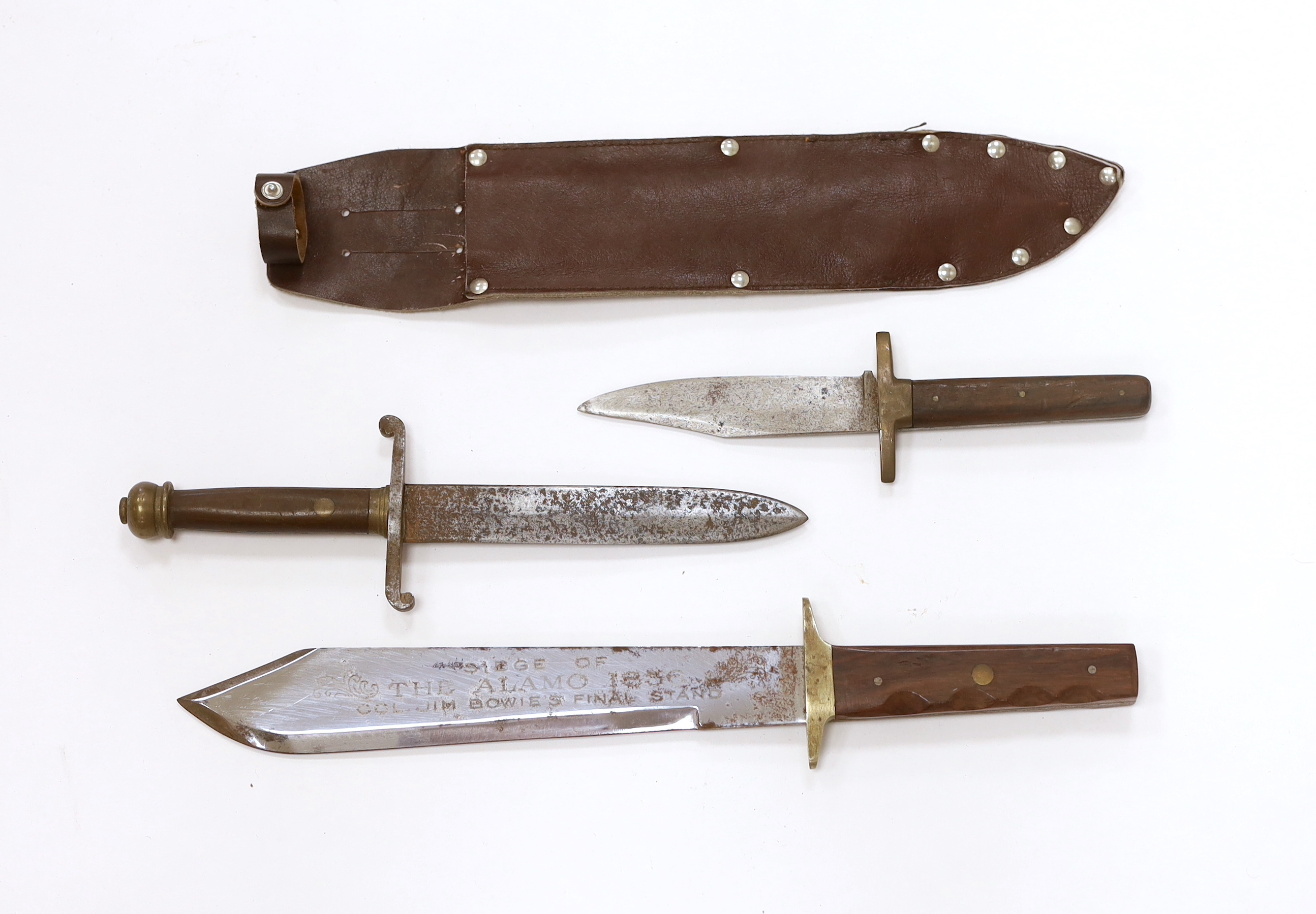 A Bowie knife with wooden grip, in a leather sleeve, blade etched with ‘Siege of The Alamo 1836 Col. Jim Bowie’s final stand’, blade 26.5cm, together with two smaller knife daggers (3)